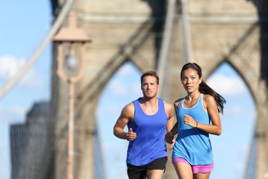 New York city runners running training for marathon on Brooklyn bridge NYC in urban cityscape. Fit young couple doing their workout routine on a summer day.