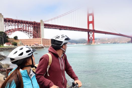 Golden gate bridge - biking couple sightseeing in San Francisco, USA. Young couple tourists on bike guided tour enjoying famous travel landmark in California, USA.