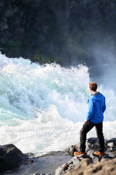 Iceland tourist looking at dramatic river by waterfall Godafoss. Man hiker on travel visiting tourist attractions and landmarks in Icelandic nature on Ring Road, Route 1.