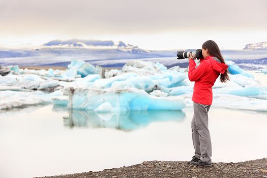 Nature landscape photographer taking picture photos with SLR camera on Iceland Jokulsarlon glacial lagoon / glacier lake. Woman taking photograph of beautiful Icelandic nature with Vatnajokull.