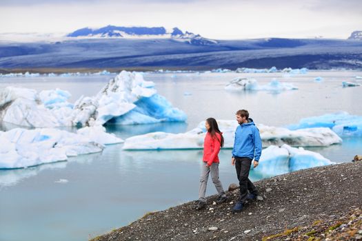 People hiking on Iceland Jokulsarlon glacial lagoon / glacier lake. Active lifestyle couple tourists walking enjoying beautiful Icelandic nature landscape with Vatnajokull in backround.