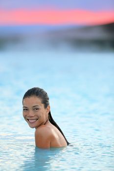 Geothermal spa. Woman relaxing in hot spring pool on Iceland. Girl enjoying bathing in a blue water lagoon Icelandic tourist attraction. Portrait of mixed race Asian Caucasian female model at sunset.