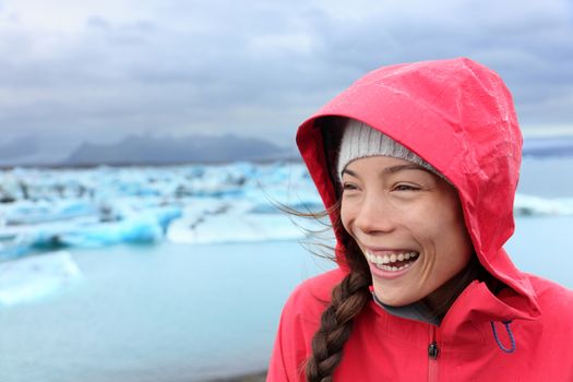 Outdoors Woman in hardshell raincoat jacket at glacier lagoon on Iceland. Happy smiling tourist girl enjoying view of Jokulsarlon glacial lake beautiful Icelandic nature landscape with icebergs.