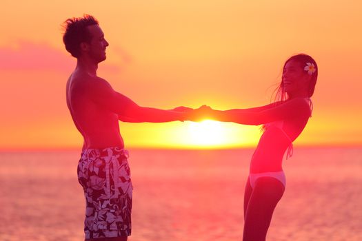 Romantic couple in swimwear having fun on beach sunset during travel. Happy woman and man holding hands playful on honeymoon romance in beautiful sunlight. Multiracial couple in Hawaii.