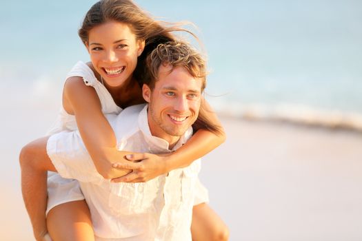 Lovers couple in love having fun dating on beach portrait. Beautiful healthy young adults girlfriend piggybacking on boyfriend hugging happy. Multiracial dating or healthy relationship concept.