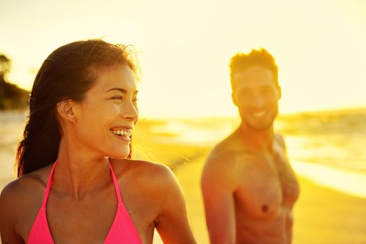 Happy multicultural couple on beach vacations. Hawaii holidays in sunset, young healthy adults together laughing walking in summer day. Asian mixed race woman, Caucasian man.