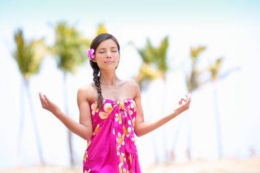 Happy Asian woman meditating on Hawaiian palm beach in sarong, hands up. Beautiful mixed race female model enjoying sun in worship and meditation zen. Big Island, Hawaii, USA.