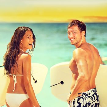 Surfers on beach having fun in summer. Surfer woman and man with boogieboard smiling happy on beach on Hawaii. Multiracial couple Asian woman and Caucasian man in outdoor water activity during travel.