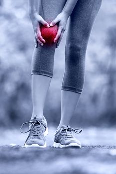 Knee injury - runner with sprained leg joint pain. Closeup of female athlete's leg with red circle showing pain. Woman holding with hands around hurting knee in summer nature background.