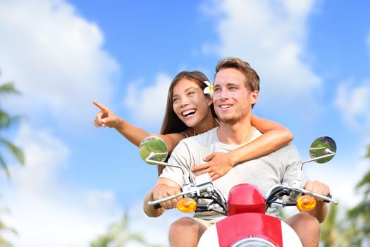 Happy couple pointing on scooter travel vacation. Young Asian woman showing her boyfriend a location while driving a moped on a road trip during summer holidays with blue sky and clouds background.