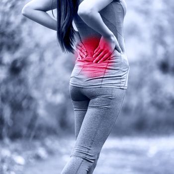 Sport woman hurting back problem - muscle pain injury. Active athlete runner massaging painful lower back because of hernial disc accident or muscular discomfort. Unrecognizable person in outdoors.