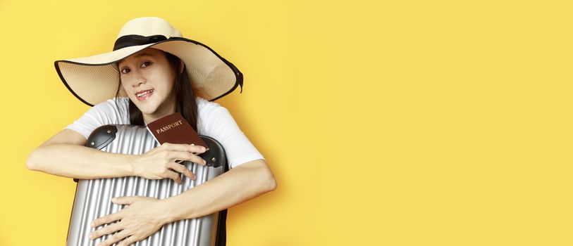 Asian women long hair wear Straw hat with black ribbon in hand holding passport book and travel bag with copy space banner. Young girl ready to travel with suitcase and passport on yellow background. Summer travel concept.