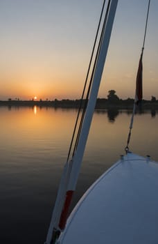 Sunset over a large river with bow of wooden sailing boat