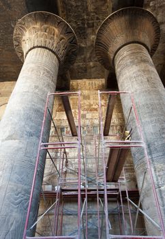 Columns in the ancient egyptian temple of Khnum at Esna with hieroglyphic carvings and scaffolding for restorations