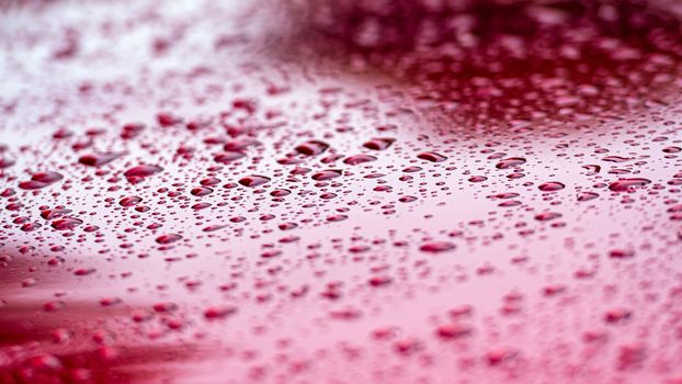 A close-up of water droplets on a red car body.