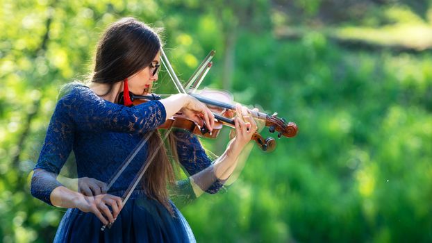 Creative composition. Young woman playing the violin at park. Shallow depth of field.