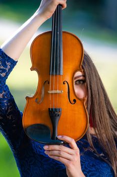 Portrait of a positive young woman. Part of the face is covered by the neck of the violin.