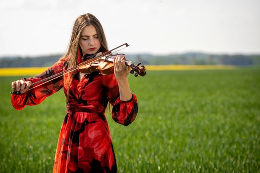 Young woman in red dress playing violin in green meadow.