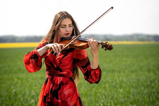 Young woman in red dress playing violin in green meadow.