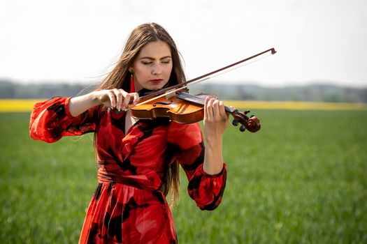 Young woman in red dress playing violin in green meadow.