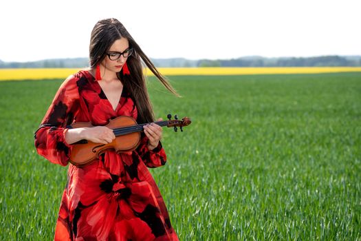 Young woman in red dress playing violin in green meadow.