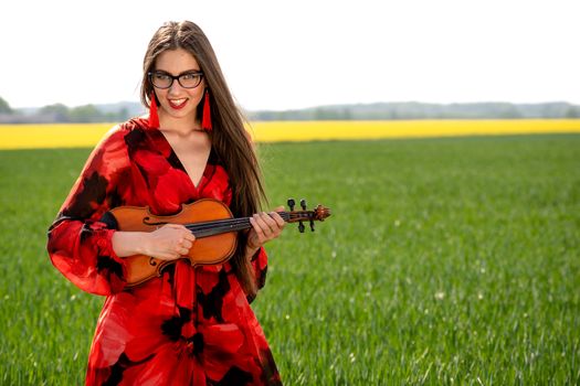 Young woman in red dress playing violin in green meadow.