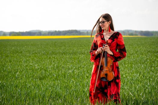 Young woman in red dress playing violin in green meadow.