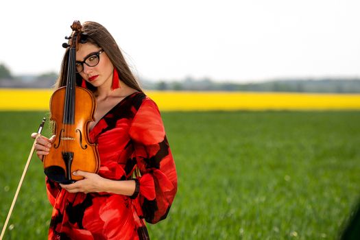 Young woman in red dress with violin in green meadow.