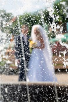 Behind the water fountain seen the groom and the bride.