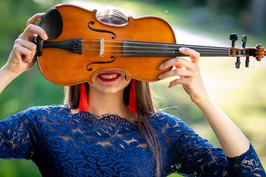 Portrait of a positive young woman. Part of the face is covered by the neck of the violin.