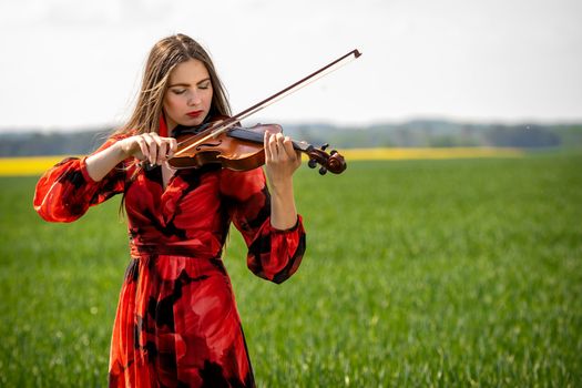 Young woman in red dress playing violin in green meadow.