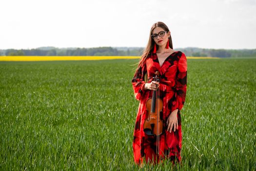 Young woman in red dress playing violin in green meadow.