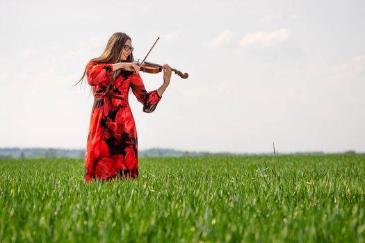 Young woman in red dress playing violin in green meadow.