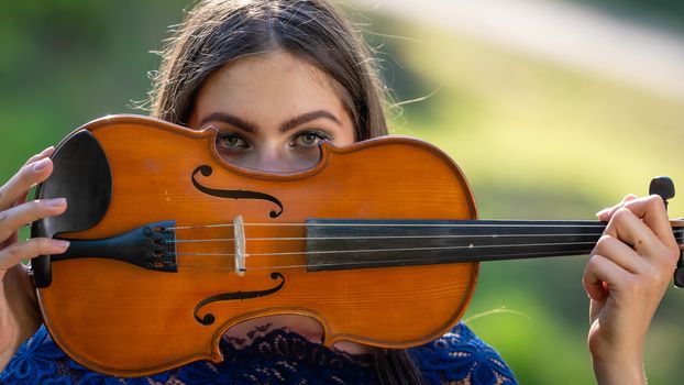 Portrait of a positive young woman. Part of the face is covered by the neck of the violin.