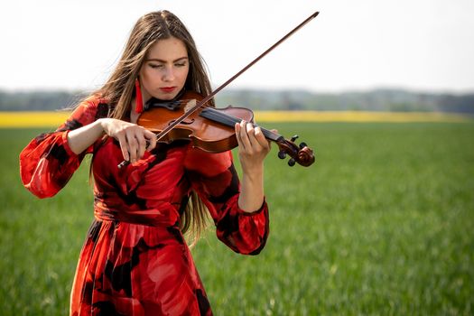 Young woman in red dress playing violin in green meadow.