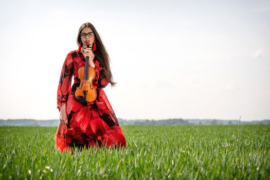 Young woman in red dress with violin in green meadow.