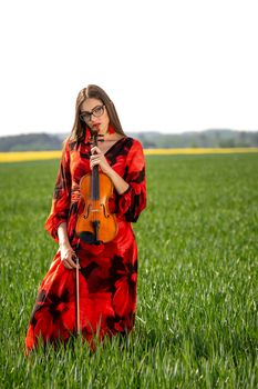 Young woman in red dress with violin in green meadow.