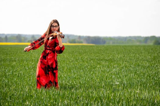 Young woman in red dress playing violin in green meadow.