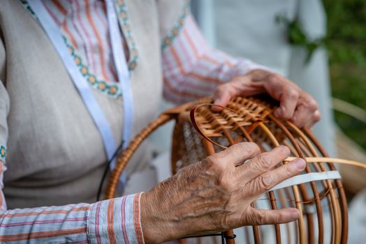 Old woman in national costume make local wicker basket. Traditional handicrafts concept. Latvia - Image