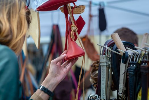 A woman in the craft market looks at red shoes. - image