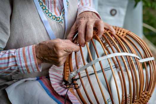 Old woman in national costume make local wicker basket. Traditional handicrafts concept. Latvia - Image