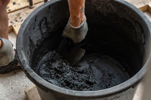 Mans hand hold a trowel and mixed cement in bucket.