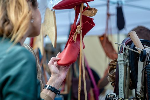 A woman in the craft market looks at red shoes. - image