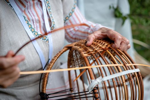 Old woman in national costume make local wicker basket. Traditional handicrafts concept. Latvia - Image