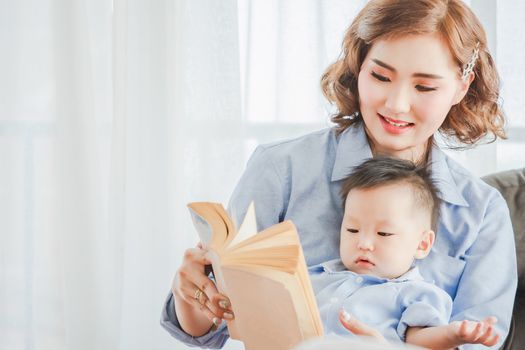 Asian Mother and child are reading a book wearing blue shirt posing for in bedroom in white room.To keep memories moment cuteness of son in childhood family lifestyle