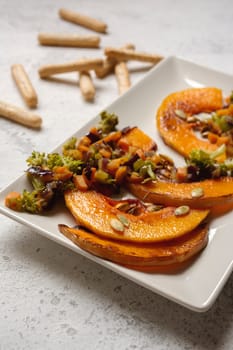 sliced baked pumpkin, with broccoli and assorted vegetables, on rectangular white plate