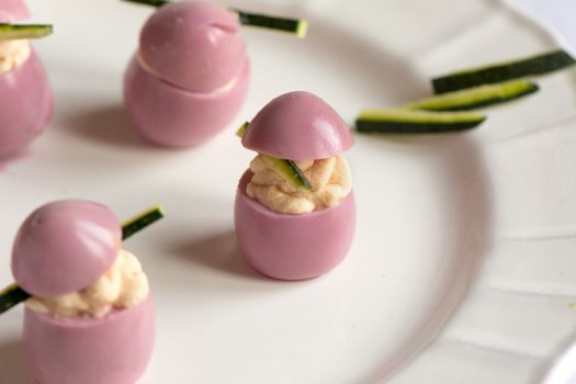 deviled quail eggs with cream cheese, dyed with beet juice, on withe plate