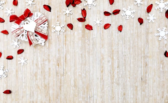 Flat lay shabby Christmas copy space with white wooden snowflakes, red petals and a white wooden decorative heart in the upper left corner on light wooden background