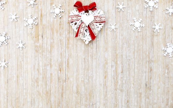 Flat lay shabby Christmas copy space with white wooden snowflakes and a white wooden decorative heart in the upper center side on light wooden background