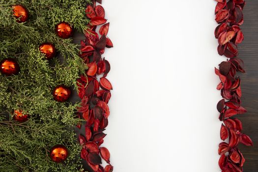 Flat lay Christmas copy space with pine branches, red Christmas baubles on one side and red petals bordering a white background